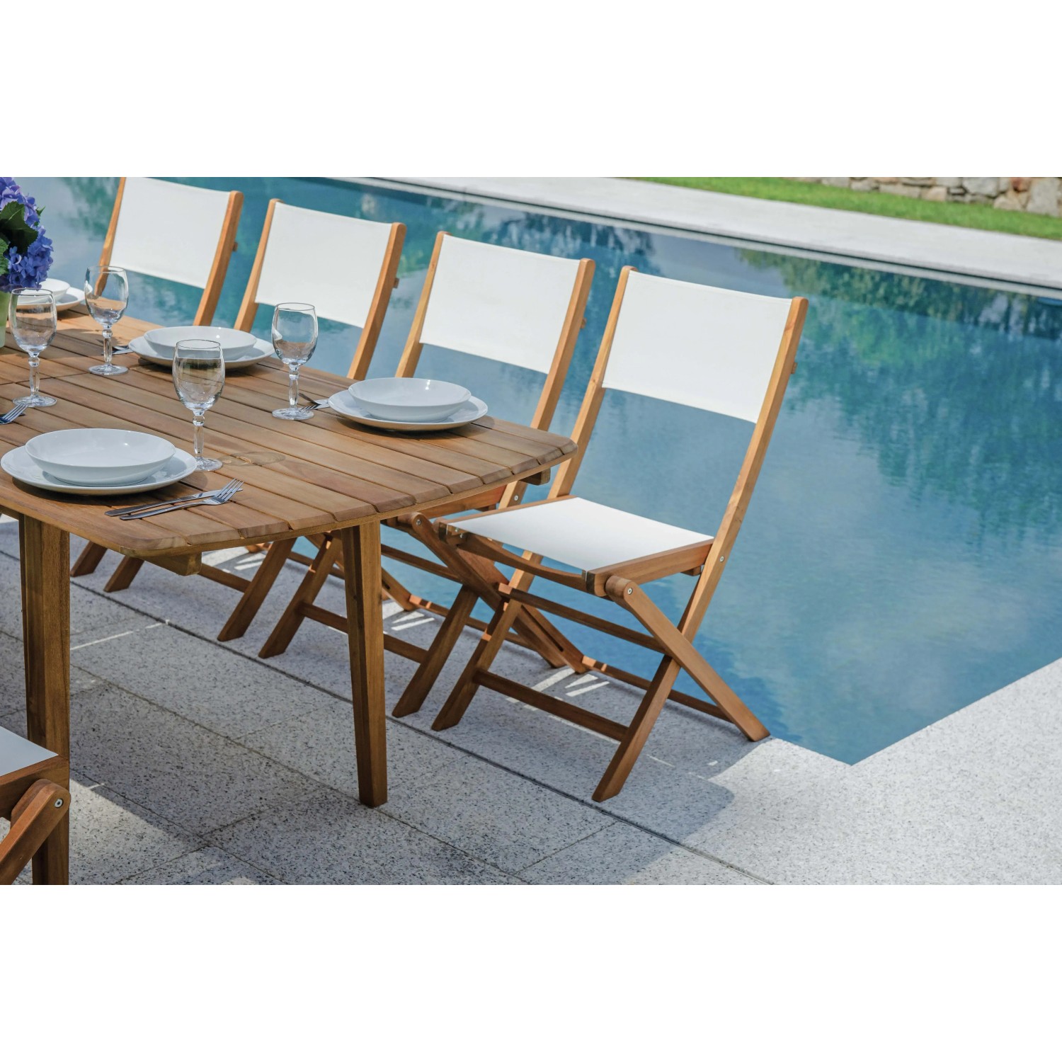 Tavolo da giardino in legno con sedie a bordo piscina, apparecchiato con stoviglie.