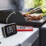 Base display Weber Smart Hub nero-argento con sensore temperatura e smartphone vicino al barbecue.