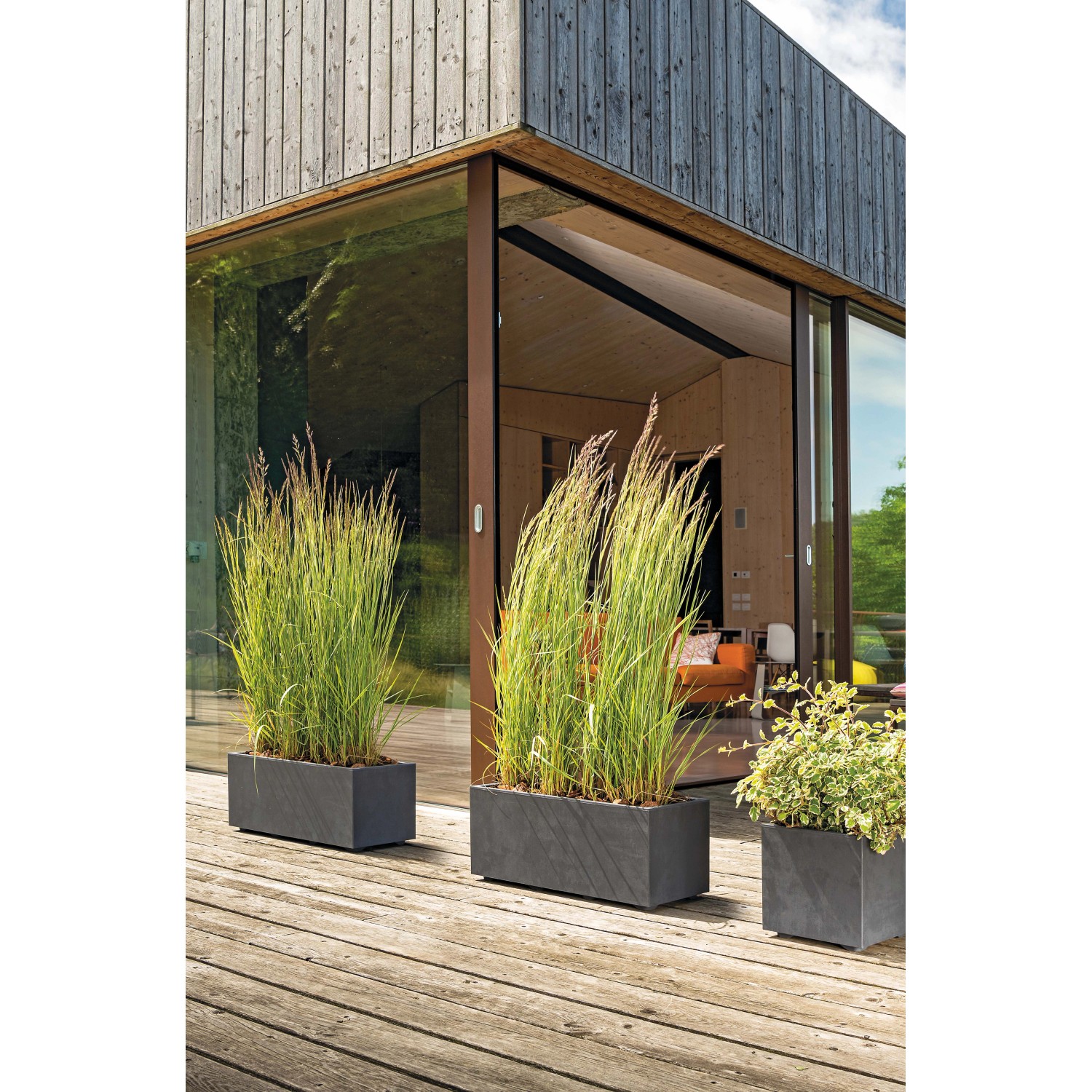 Fioriera antracite Deroma Millennium con piante su una terrazza di legno.