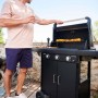 Barbecue a gas nero con uomo che griglia spiedini in giardino.