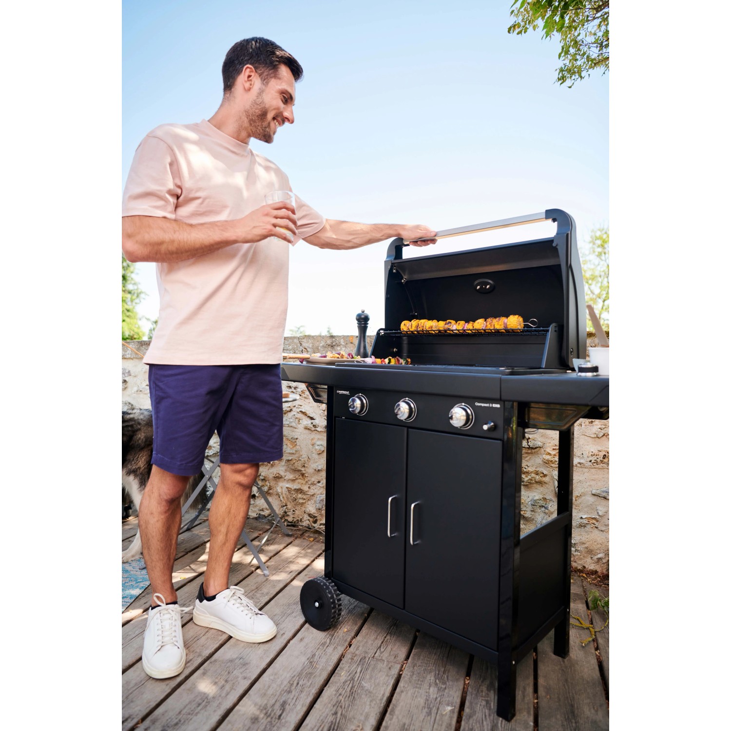 Barbecue a gas nero con uomo che griglia spiedini in giardino.