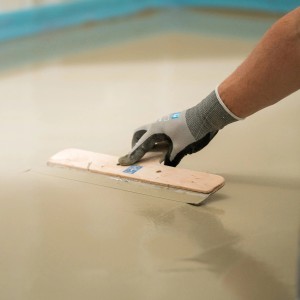 Artigiano che stende autolivellante Mapei (3-30 mm) sul pavimento con una spatola lisciante.