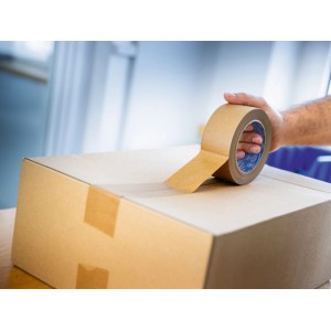 Mano applica nastro adesivo di carta marrone su scatola di cartone. Ideale per imballaggio e spedizioni sicure.