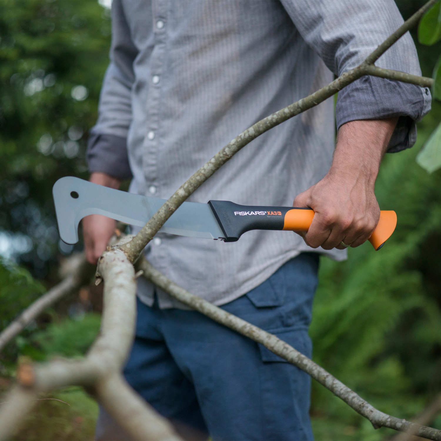 Machete Fiskars WoodXpert XA3 in azione: uomo taglia ramo con la sega da giardino.