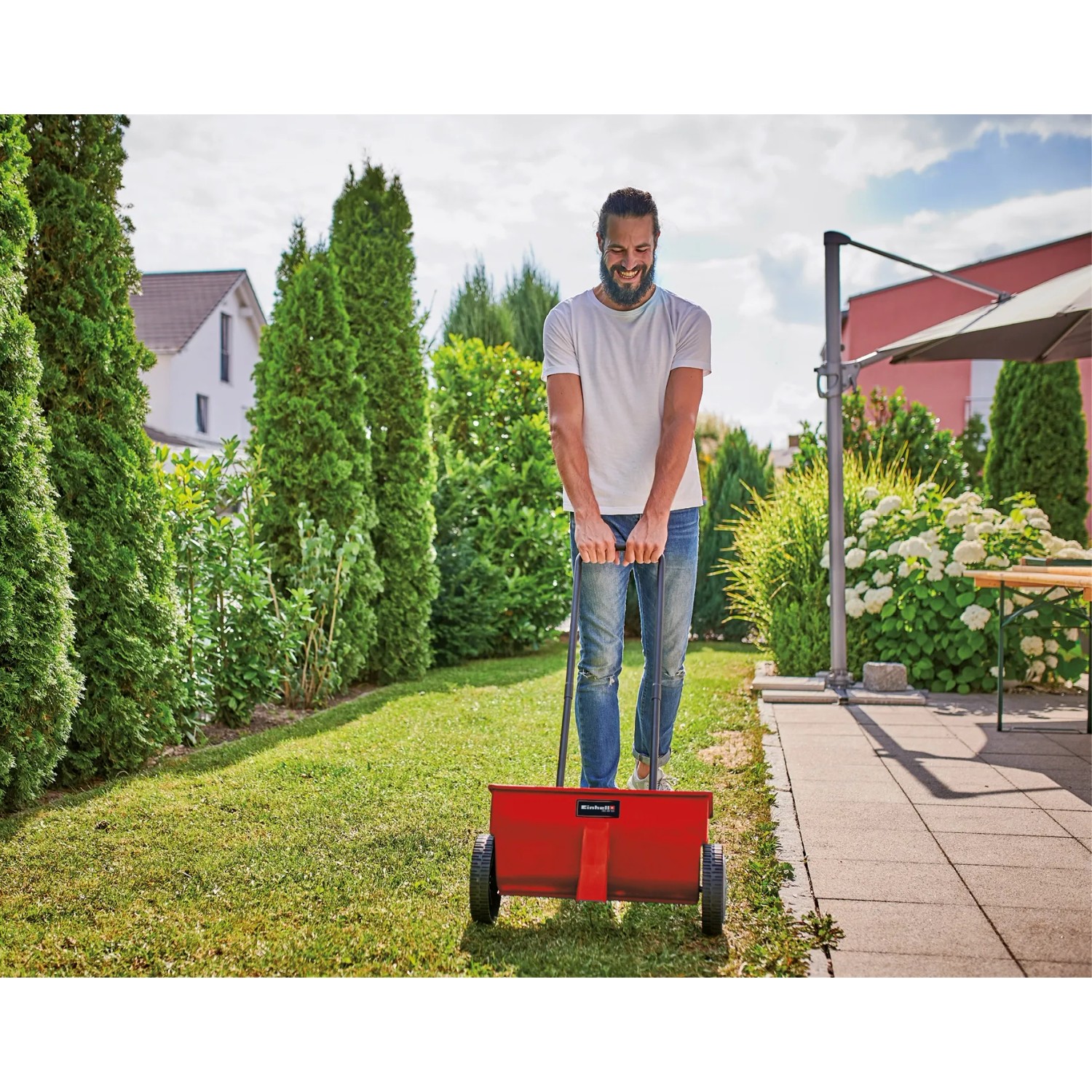 Spargitore Einhell GC-SR 12 in uso: uomo spinge spargitore di fertilizzante rosso su prato in giardino.