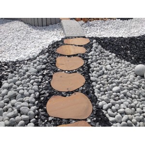 Sentiero da giardino in pietra naturale in un letto di ghiaia con ciottoli decorativi bianchi e grigi.