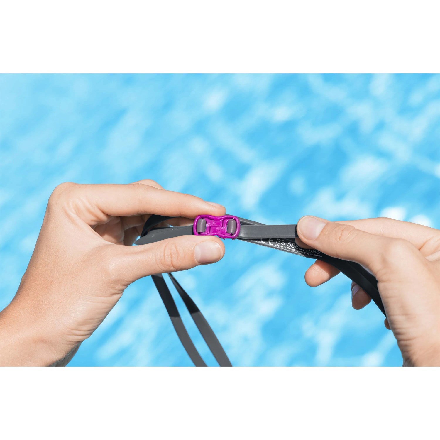 Occhialini da nuoto grigi con chiusura rosa, tenuti da due mani.