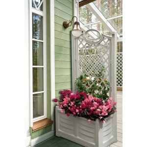 Fioriera da esterno con grigliato e fiori rosa davanti a una parete verde.