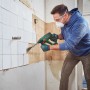 Uomo che rimuove piastrelle con il martello perforatore a batteria Bosch UniversalHammer 18V. Trapani a percussione per il fai da te.