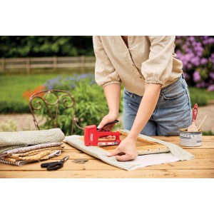 Donna che utilizza una cucitrice rossa per fissare il tessuto su una cornice di legno.