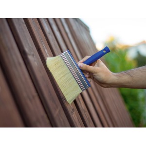 Mano che dipinge una staccionata di legno con un pennello largo.
