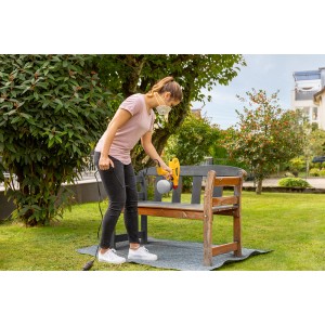 Donna che spruzza una panca di legno con il sistema di verniciatura Wagner W 125 in giardino.