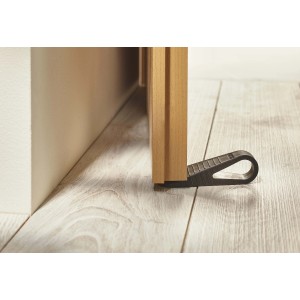 Fermaporta nero t.b.t. in plastica che blocca una porta di legno su pavimento in legno chiaro.