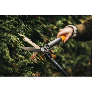 Cesoie per siepi Fiskars PowerGearTM II HS72 tagliano una siepe. Cesoie da giardino con manico nero e dettagli arancioni.