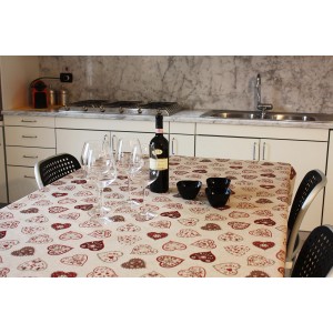 Tavolo con tovaglia t.b.t. con motivo a cuore, bicchieri e bottiglia di vino.