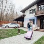 Casa con auto parcheggiata e coppia con valigia. Videosorveglianza per il monitoraggio della proprietà.