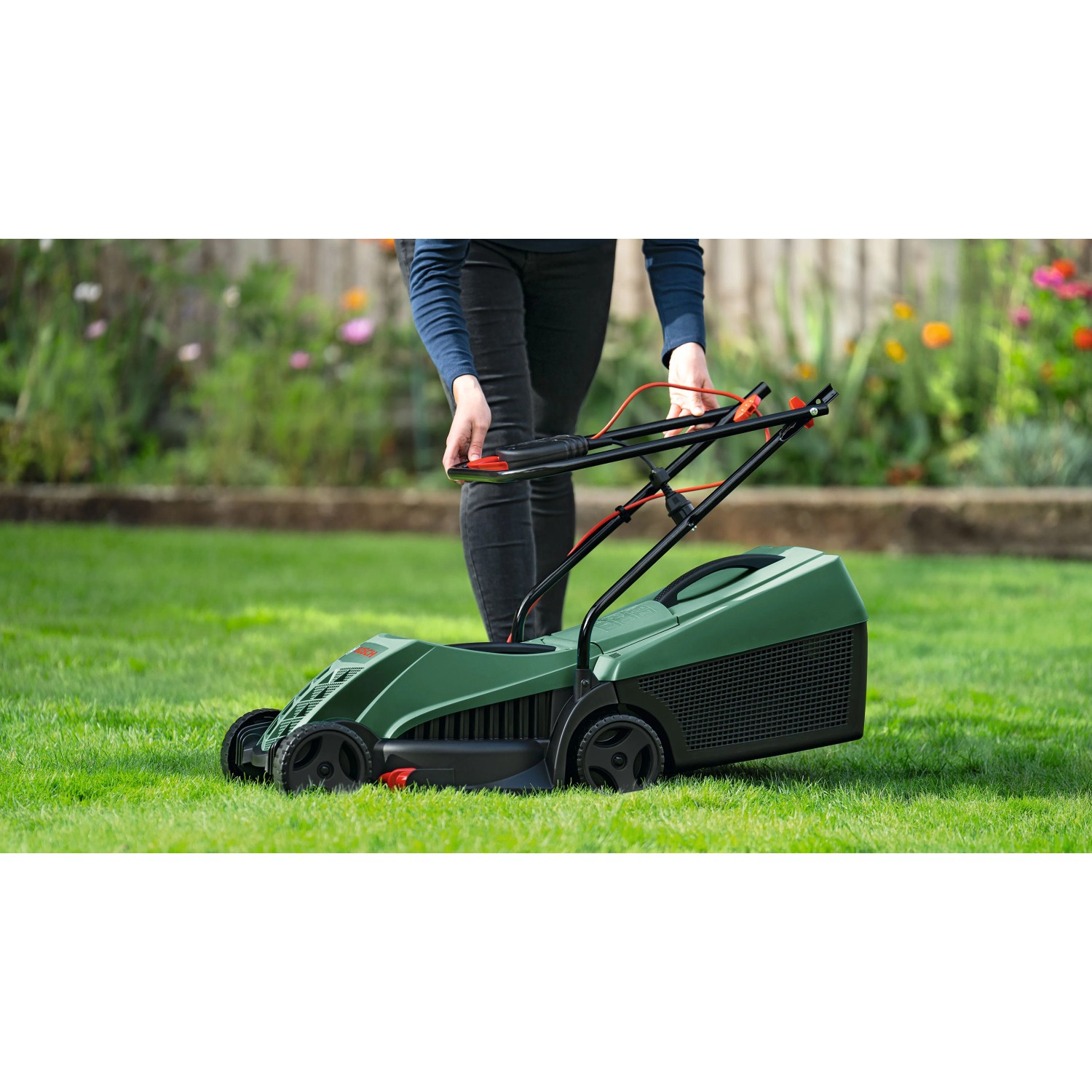 Persona taglia prato con tosaerba elettrico Bosch Easy Rotak 32-215 verde. Maniglie pieghevoli per facile uso in giardino.