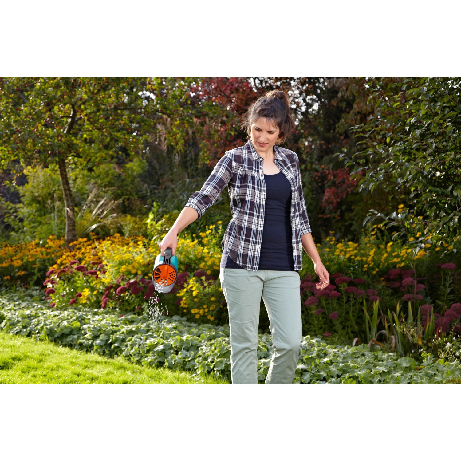 Donna che sparge fertilizzante con lo spargitore Gardena Small S Turchese in giardino.