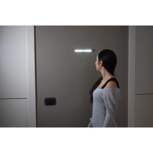 Donna guarda la barra luminosa a LED t.b.t. su parete grigia. Soluzione di illuminazione moderna.