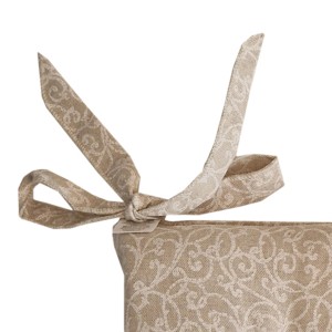 Dettaglio di un cuscino beige con motivo floreale e lacci.