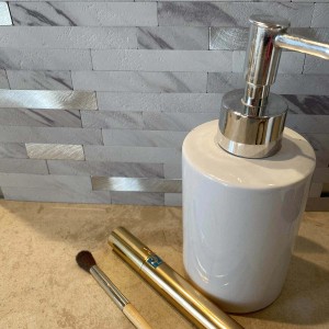 Alzatina piastrellata Mosaico chiara con dispenser di sapone bianco e prodotti cosmetici.