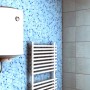 Scaldabagno bianco su parete a mosaico blu, accanto a scaldasalviette. Tasselli.