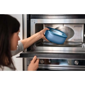 Donna mette contenitore t.b.t. blu nel microonde. Pratico contenitore per cucina.