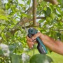 Forbici da giardino a batteria Gardena Assistcut in uso su un albero con foglie verdi e frutti.