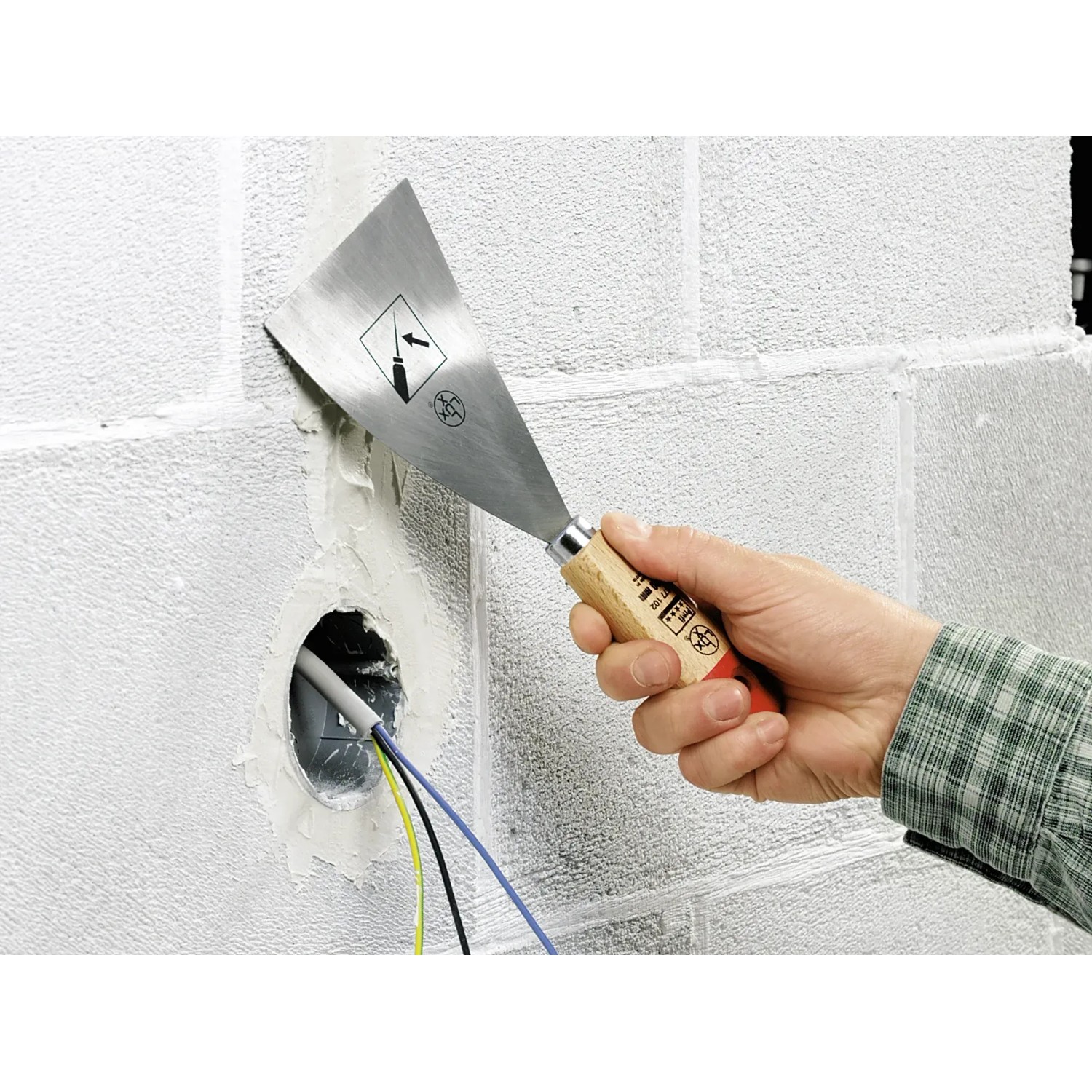 Mano che tiene spatola LUX rigida (100mm) per lisciare lo stucco su una parete.