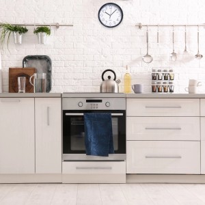 Orologio da parete in cucina con mobili bianchi e forno. Segnatempo per la cucina.