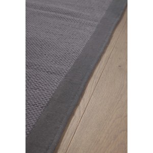 Dettaglio di uno stuoia t.b.t. grigio con bordo su pavimento in legno.