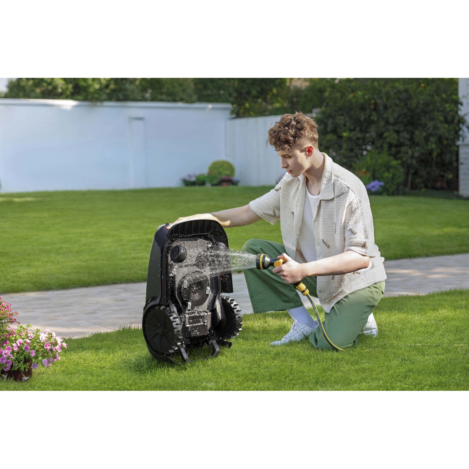 Uomo pulisce un robot tagliaerba t.b.t. nero con un tubo dell'acqua in giardino.