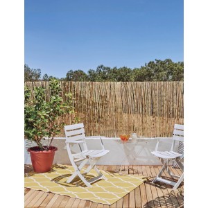 Scena con paravista t.b.t., sedie da giardino bianche e tappeto giallo su un patio.