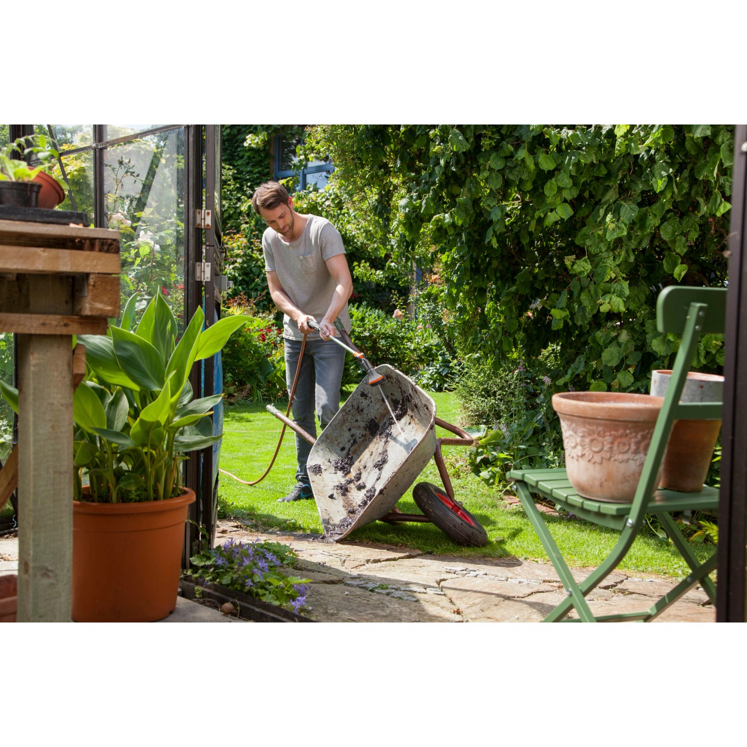 Uomo pulisce carriola con lancia per irrigazione Gardena Comfort 90 cm in giardino.