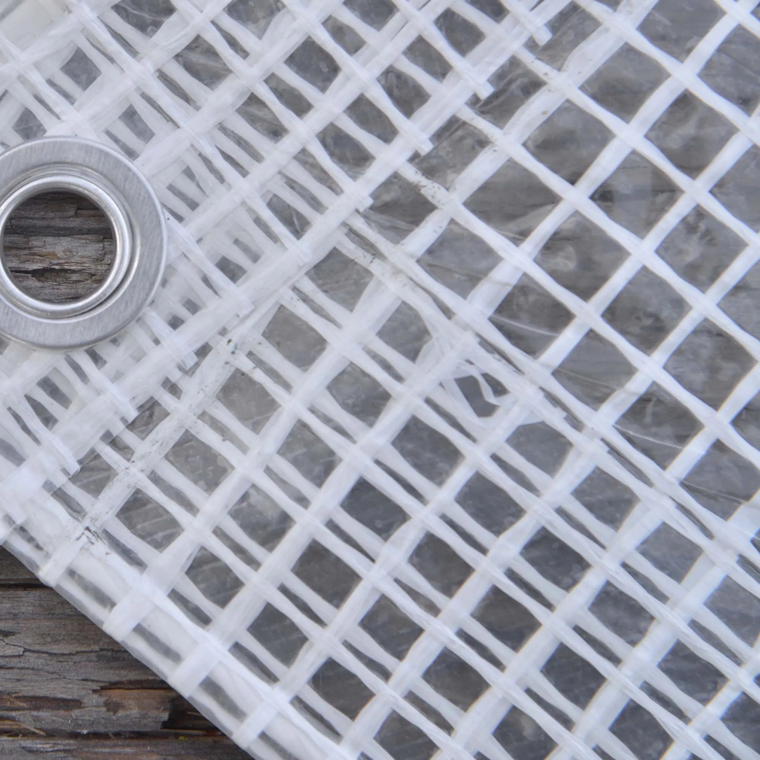 Dettaglio di un telo di copertura trasparente con occhiello e struttura a griglia.