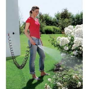 Donna che annaffia il giardino con tubo a spirale e pistola a spruzzo.