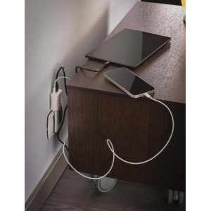 Adattatore multiplo con tablet e smartphone in carica su un comodino.