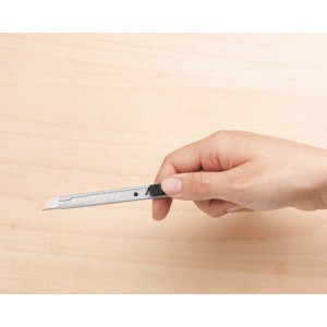 Mano che tiene un cutter LUX da 9 mm con corpo in metallo su legno chiaro.