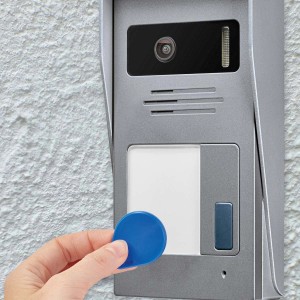 Mano che tiene chip blu davanti al citofono grigio con telecamera.