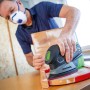 Uomo che leviga il legno con levigatrice multifunzione a batteria LUX A-MS-20. Levigatrice senza fili per legno e metallo.