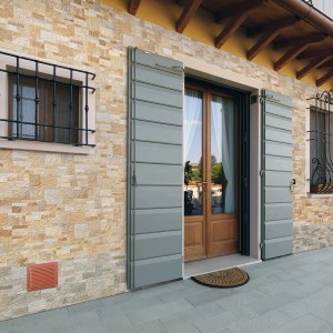 Vista esterna di una casa con finestra, porta e una griglia di ventilazione t.b.t. marrone.