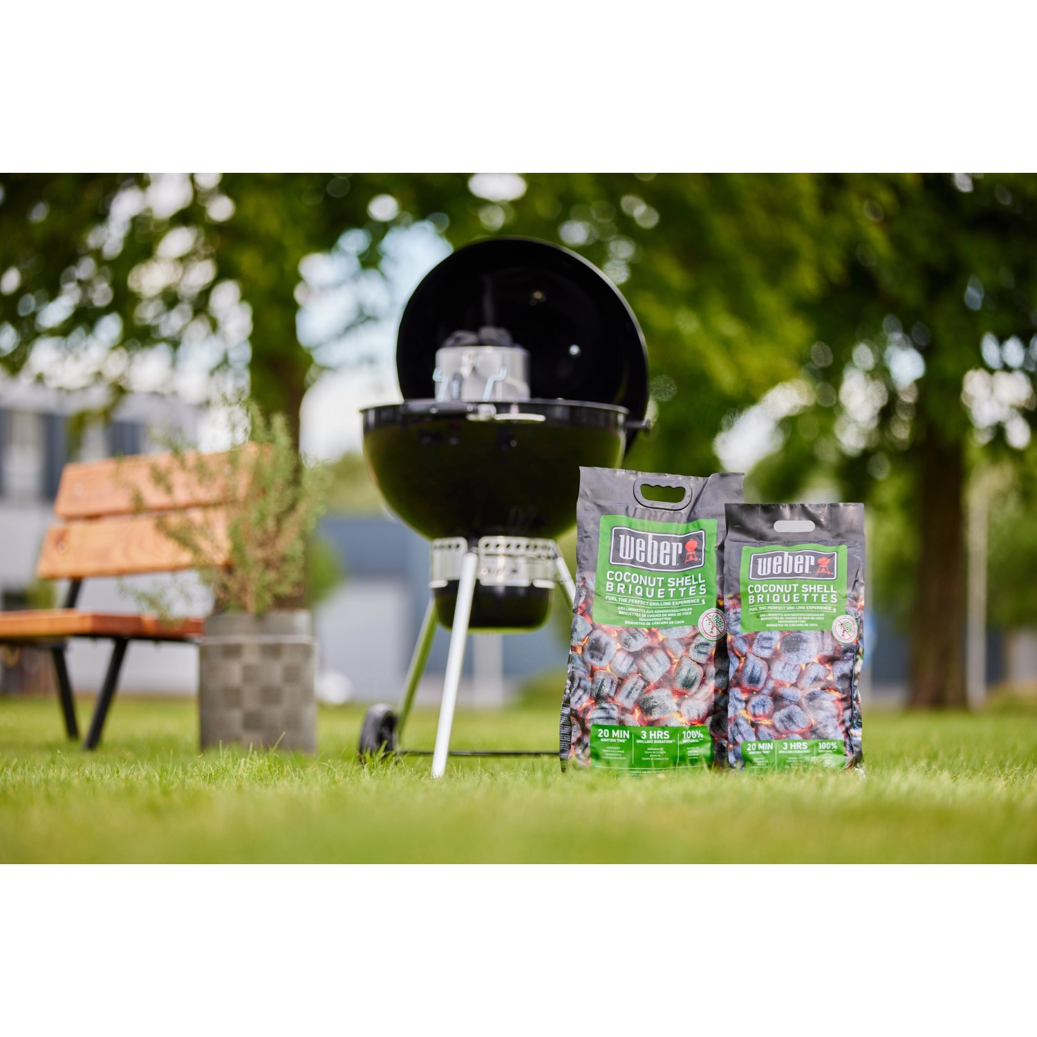 Weber Bricchetti di cocco 4 kg con barbecue sullo sfondo. Combustibile per grigliate a lunga durata.