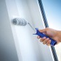 Rullo per pittura LUX 12cm in uso: rullo con manico blu che dipinge una parete bianca.