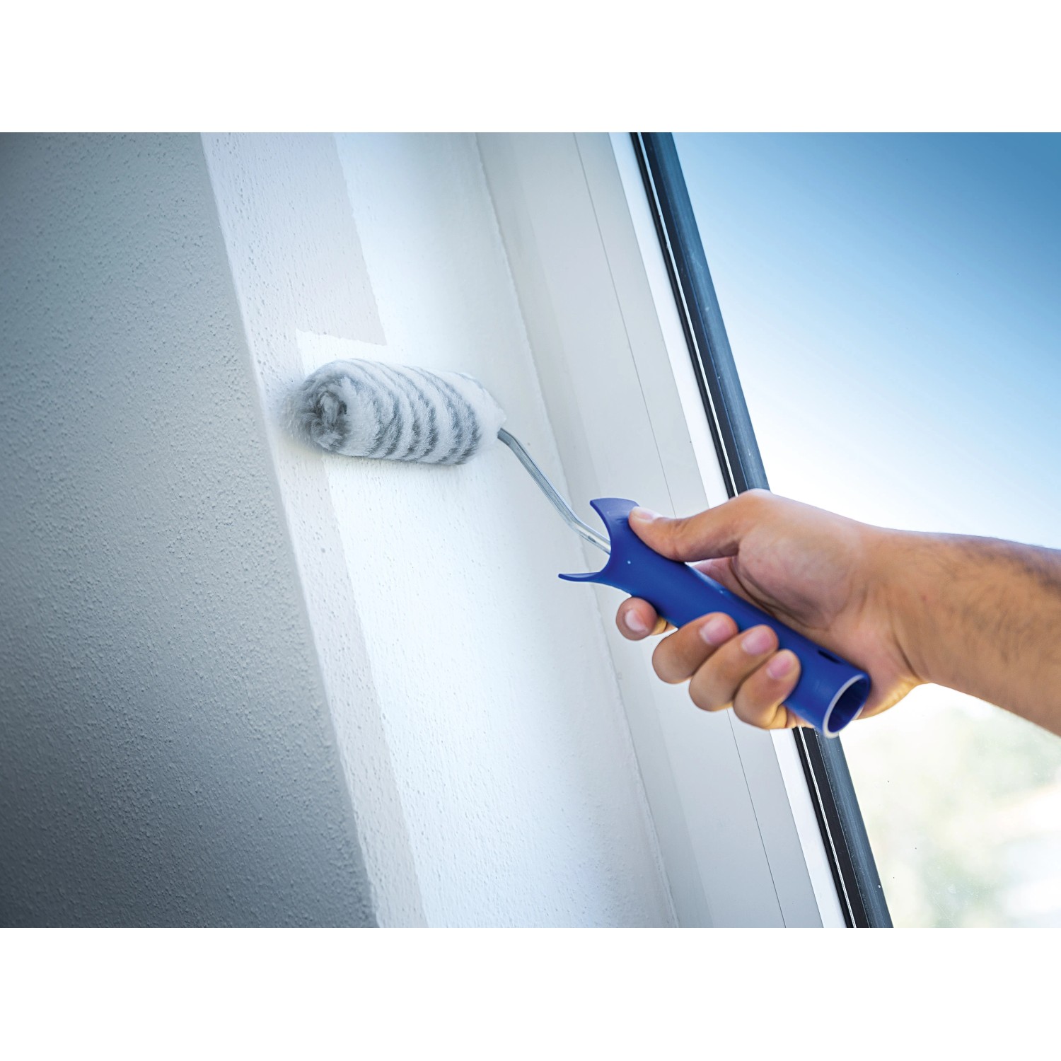 Rullo per pittura LUX 12cm in uso: rullo con manico blu che dipinge una parete bianca.