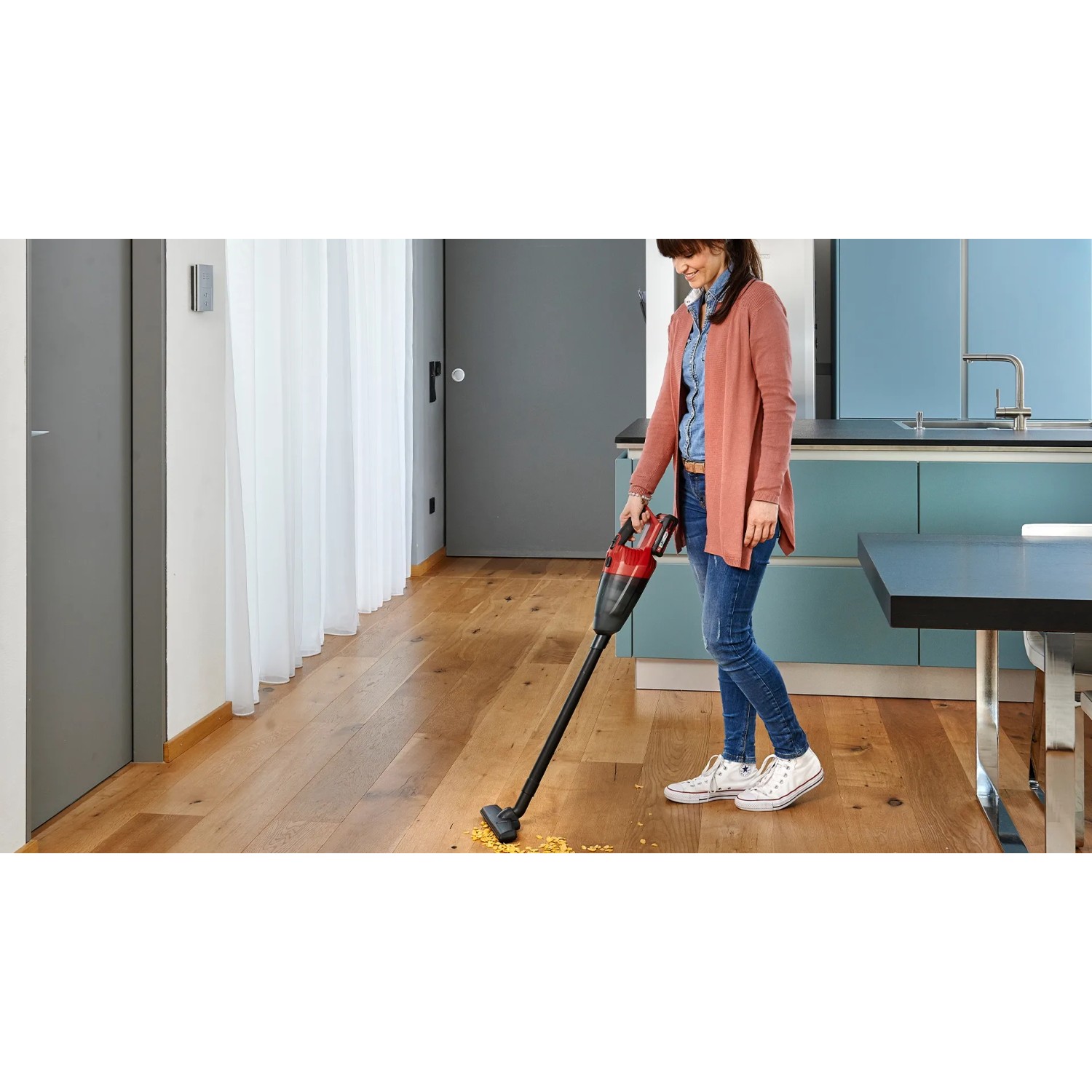 Donna aspira briciole sul parquet con l'aspirapolvere a batteria Einhell TE-VC 18 Li Solo.