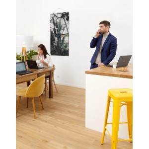 Pavimento vinilico chiaro in soggiorno con persone e sgabello giallo.