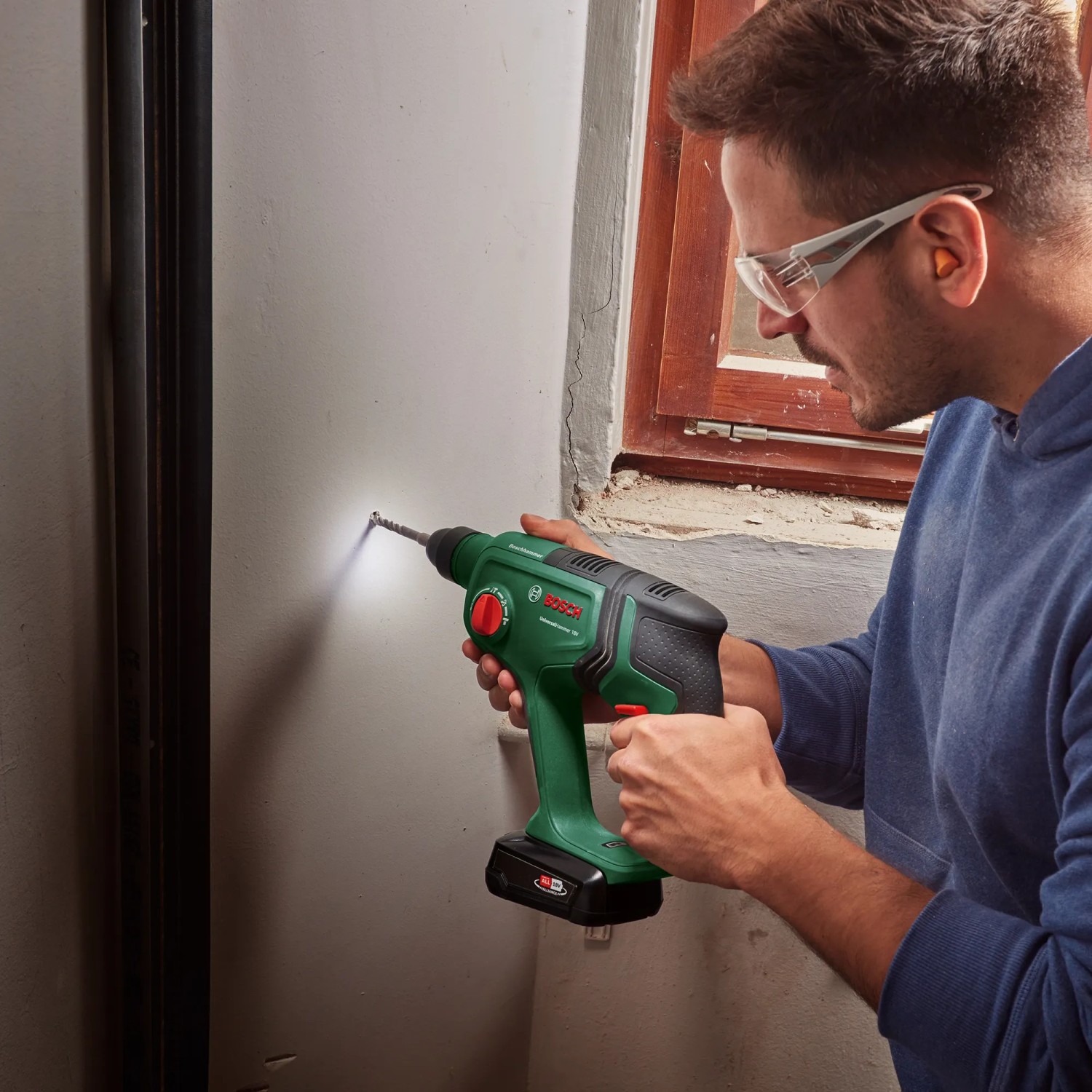 Uomo che fora un muro con il trapano a percussione a batteria Bosch UniversalHammer 18V. Include luce LED.