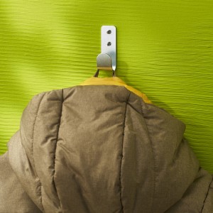 Giacca appesa a un gancio a muro color argento su una parete verde.