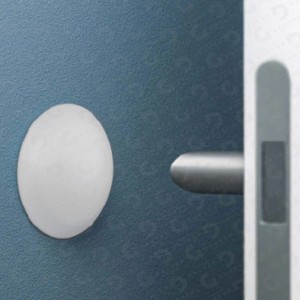 Fermaporta (Fermaporte) bianco rotondo di t.b.t. su una parete blu accanto a una maniglia.