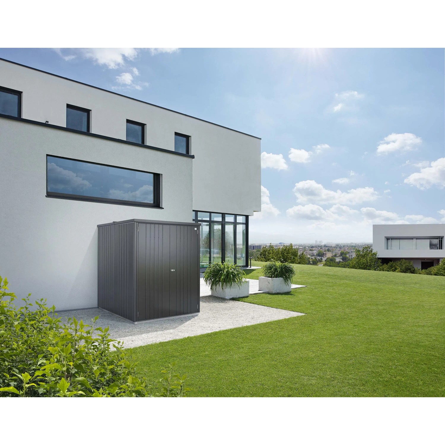 Armadio da esterno Biohort Large, grigio scuro metallizzato, davanti a casa moderna su prato.